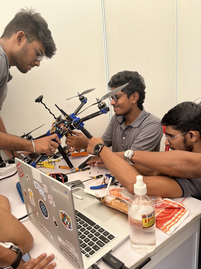 Three people assembling and wiring a hexacopter at a workbench